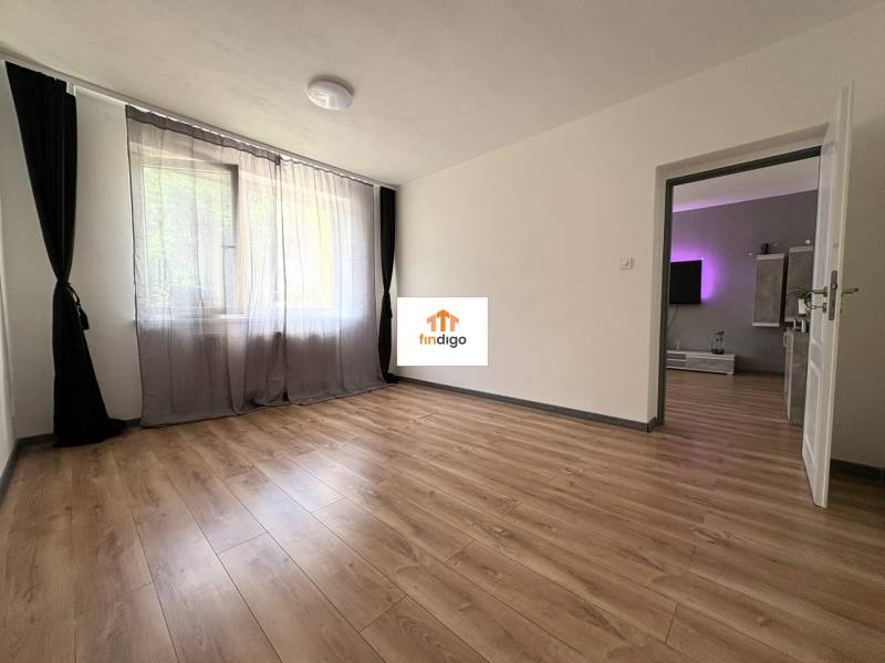 PREDAJ-  2 izbový byt neďaleko Nitry v obci Jarok - Priestranná izba s drevenou podlahou a závesmi v 2-izbovom byte.