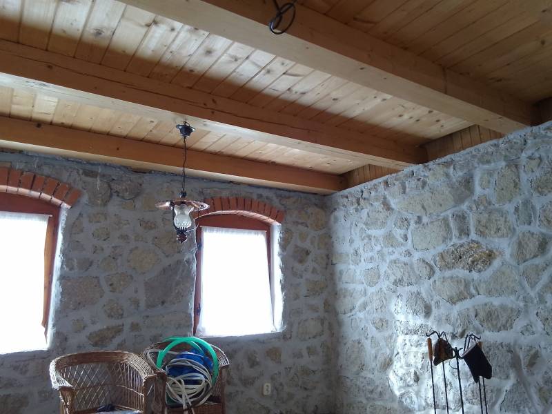 Štýlový rekreačný domček Levice - Kamenné steny chaty s dreveným stropom, dvomi oknami a prútenými stoličkami.