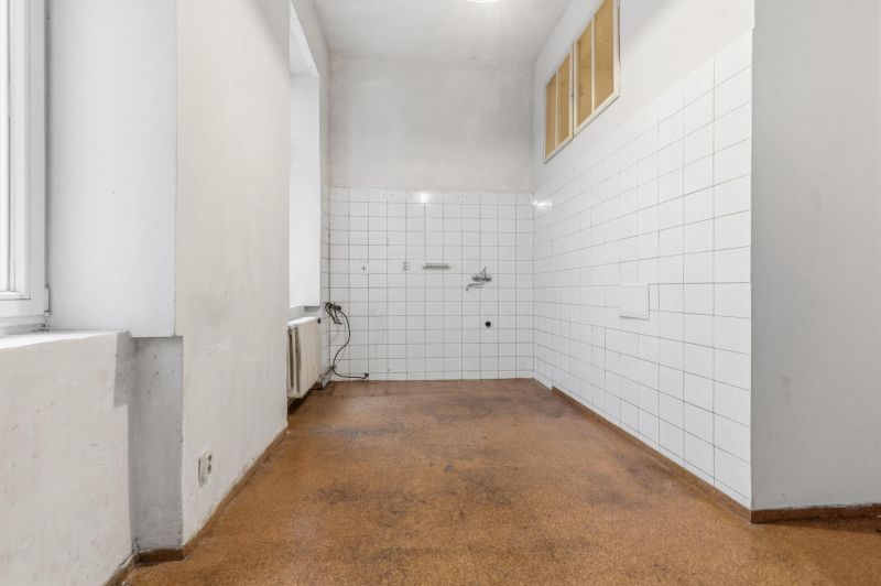 3- izb. byt o výmere 105m2 v historickom centre. - Prázdna miestnosť v 3-izbovom byte s bielymi dlaždicami a podlahou hnedého odtieňa.