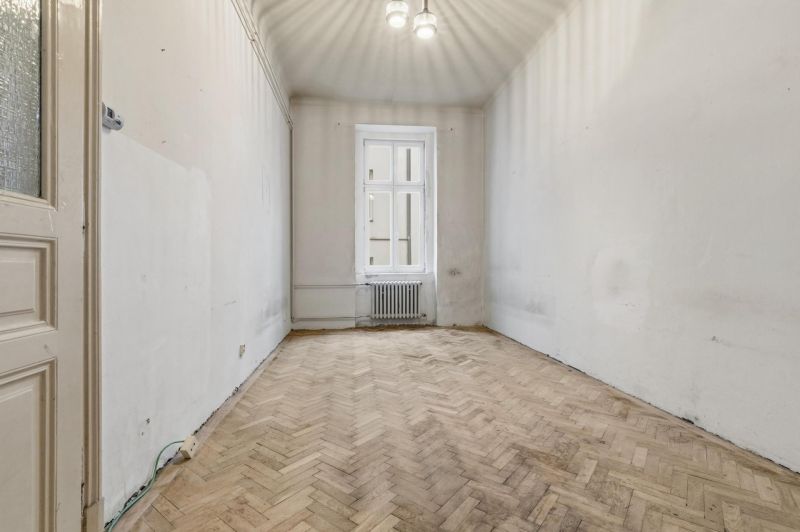 3- izb. byt o výmere 105m2 v historickom centre. - Prázdna miestnosť s podlahou s dreveným dekorom v 3-izbovom byte, jednoduchý luster.
