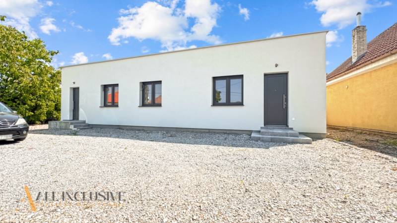 IDEÁLNY 1 IZBOVÝ BYT | VEĽKÉ RIPŇANY | TOPOĽČANY - Jednopodlažná budova s bielou omietkou a štrkovým parkoviskom na Hlohovskej ceste vo Veľkých Ripňanoch.