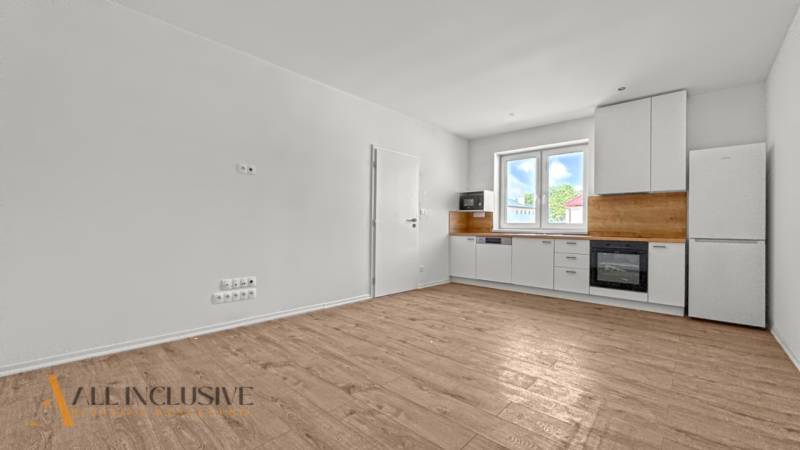 IDEÁLNY 1 IZBOVÝ BYT | VEĽKÉ RIPŇANY | TOPOĽČANY - Interiér 1-izbového bytu s kuchyňou, bielymi skrinkami a podlahou s dreveným dekorom.