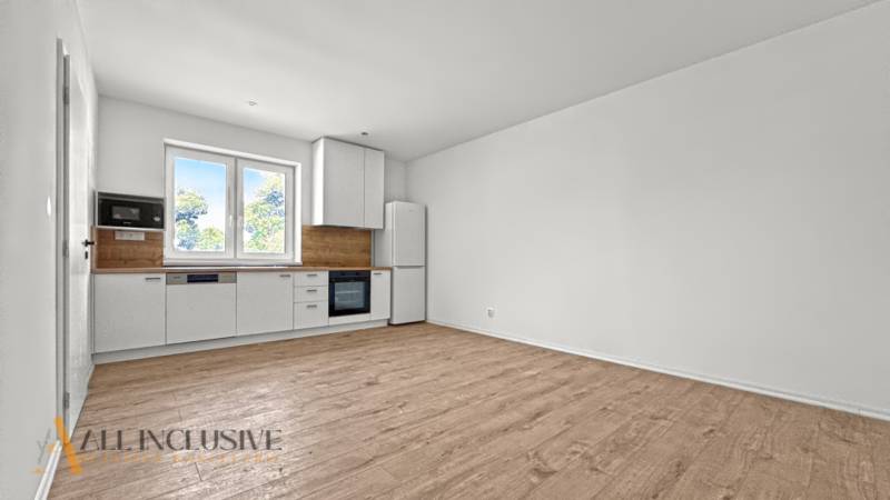 IDEÁLNY 1 IZBOVÝ BYT | VEĽKÉ RIPŇANY | TOPOĽČANY - Kuchyňa v 1-izbovom byte s bielymi skrinkami a podlahou s dreveným dekorom.