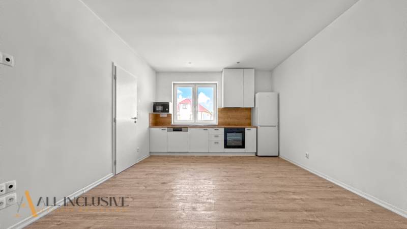 IDEÁLNY 1 IZBOVÝ BYT | VEĽKÉ RIPŇANY | TOPOĽČANY - Minimalistická kuchyňa s bielymi skrinkami a podlahou s dreveným dekorom v 1-izbovom byte.