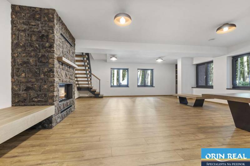 PREDAJ 8 IZB.REKREAČNEJ CHATY - VILY V MODRE HARMÓNII - Na obrázku je priestranná miestnosť s krbom, drevenými schodmi a veľkými oknami.