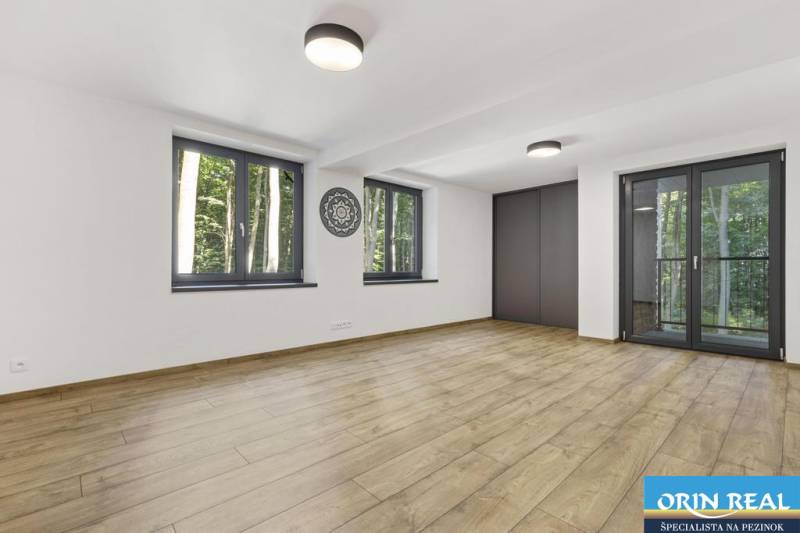 PREDAJ 8 IZB.REKREAČNEJ CHATY - VILY V MODRE HARMÓNII - Priestranná miestnosť s drevenou podlahou, veľkými oknami a výhľadom do lesa.