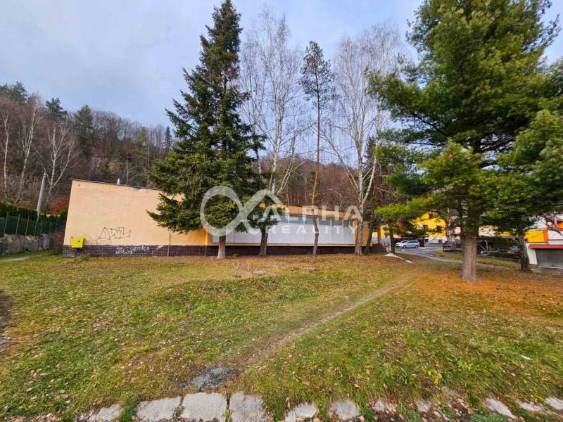 Budova s pozemkom, obec Helcmanovce, okres Gelnica - Budova v Helcmanovciach obklopená stromami, so susednou cestou a vozidlami.