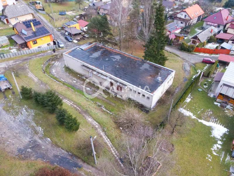 Budova s pozemkom, obec Helcmanovce, okres Gelnica - Budova v Helcmanovciach obklopená zeleňou a ďalšími domami v zasneženej krajine.