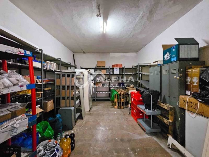 Budova s pozemkom, obec Helcmanovce, okres Gelnica - Miestnosť s regálmi, plechovými skrinkami a rôznymi predmetmi na podlahe s dreveným dekorom.