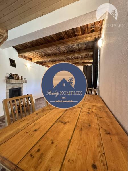 Vám ponúka na predaj rodinný dom v Komárne, ča - Interiér rodinného domu so stolom z drevom dekoru, krbom a dreveným stropom.