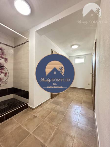 Vám ponúka na predaj rodinný dom v Komárne, ča - Chodba rodinného domu s dlažbou a sprchou s kvetinovým vzorom na stene.