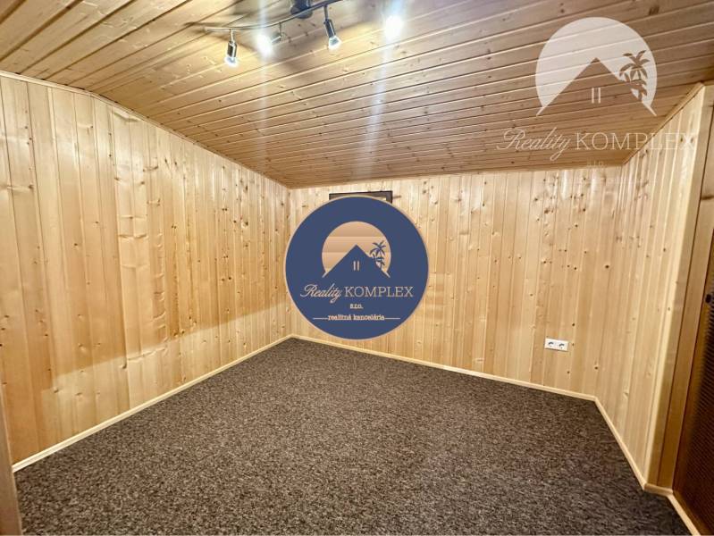 Vám ponúka na predaj rodinný dom v Komárne, ča - Izba v rodinnom dome s drevom obloženými stenami a kobercovou podlahou.