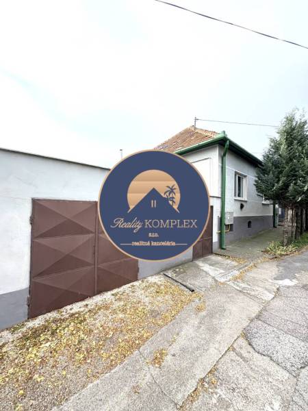 IBA U NÁS !!! ponúka EXKLUZÍVNE na predaj rodin - Rodinný dom v Komárne so zelenými detailami a hnedou bránou na tichej ulici.