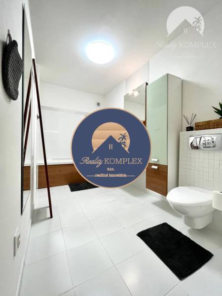 Vám EXKLUZÍVNE ponúka NA PRENÁJOM moderný 2 iz - Kúpeľňa v 2-izbovom byte s vaňou, umývadlom a toaletou na bielej dlažbe.