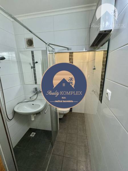 Vám ponúka 1 izbový byt vo VYHĽADÁVANEJ lokali - Kúpeľňa so sprchovým kútom a tmavou podlahou v 1-izbovom byte, biele obklady.