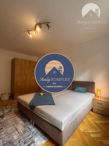 Vám ponúka 1 izbový byt vo VYHĽADÁVANEJ lokali - Spálňa v 1-izbovom byte so svetlom, skriňou a posteľou na podlahe s dreveným dekorom.