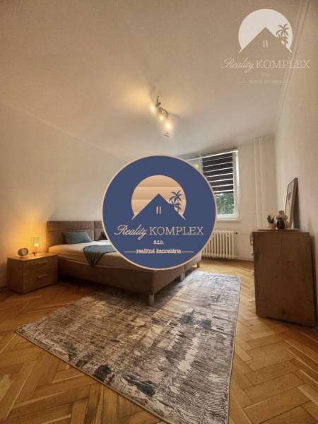 Vám ponúka 1 izbový byt vo VYHĽADÁVANEJ lokali - Svetlá izba s posteľou, kobercom a podlahou s dreveným dekorom v 1-izbovom byte.