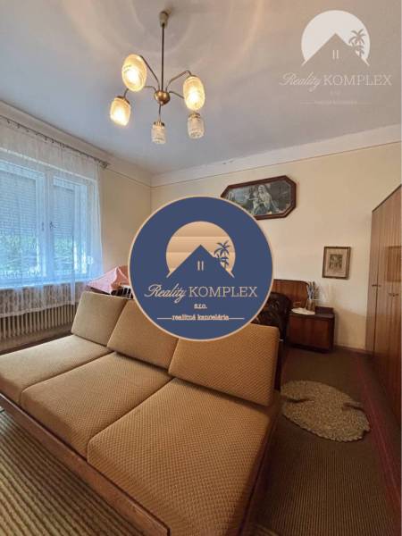 Vám ponúka na predaj 4 izbový rodinný dom  s r - Obývacia izba v rodinnom dome s pohovkou, lustrom a svetlou záclonou na okne.