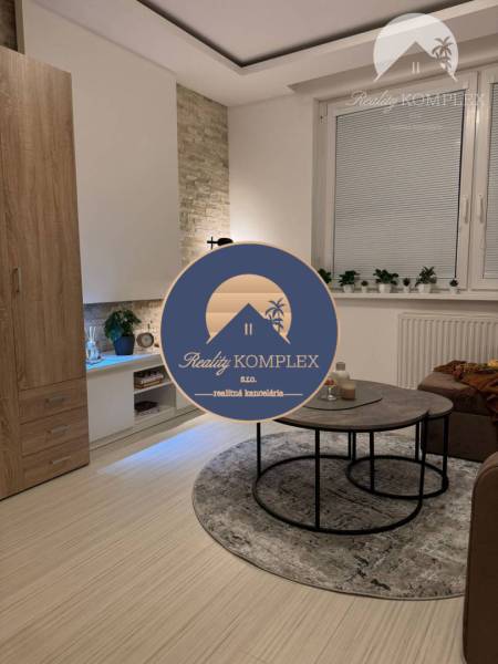 Vám ponúka garsonku vo VYHĽADÁVANEJ lokalite m - Obývacia izba s gaučom, konferenčným stolíkom a podlahou s dreveným dekorom v rekreačnom apartmáne.