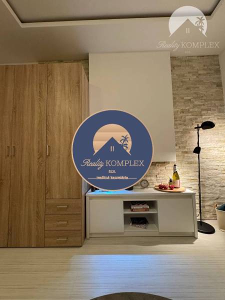 Vám ponúka garsonku vo VYHĽADÁVANEJ lokalite m - Interiér rekreačného apartmánu s podlahou s dreveným dekorom, skriňou a štýlovou lampou.