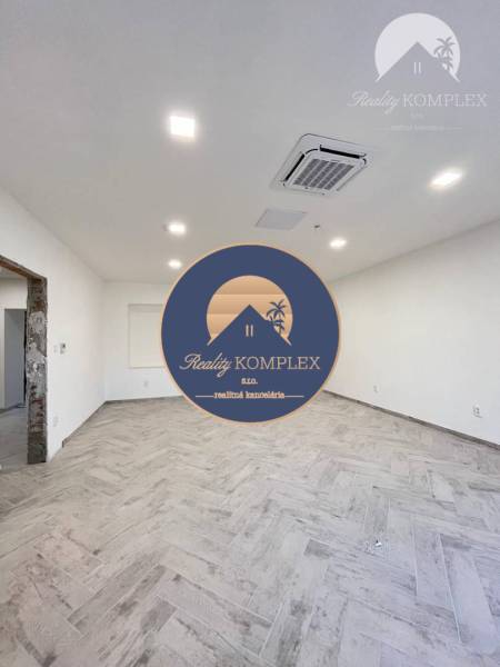 Vám ponúka  na predaj budovu na BÝVANIE aj PODN - Interiér priestrannej miestnosti s drevenou podlahou a zabudovaným osvetlením. Budova má bielu stenu.