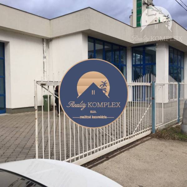 Vám ponúka do PRENÁJMU priestranné a slnečné ob - Obchodné priestory na ulici 1. mája v Hurbanove s modrými oknami za bielym plotom.