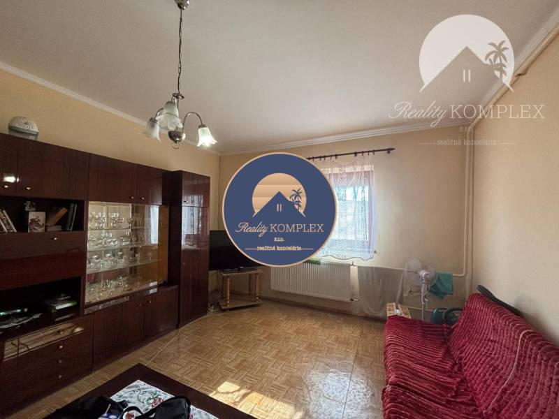 Reality KOMPLEX Vám ponúka EXKLUZÍVNE na predaj rodinný dom, ktorý sa  - Obývacia izba v rodinnom dome s podlahou s dreveným dekorom, tmavým nábytkom a červenou pohovkou.