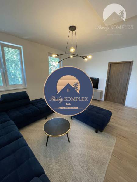 Vám ponúka na Prenájom 2-izbový byt s loggiou  - Štýlová obývacia izba s tmavým gaučom, podlahou s dreveným dekorom a oknami.