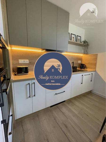 Vám ponúka na Prenájom 2-izbový byt s loggiou  - Kuchyňa v 2-izbovom byte s podlahou s dreveným dekorom a svetlým osvetlením.