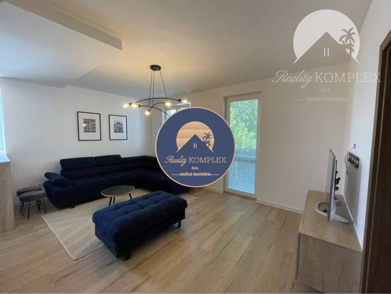 Vám ponúka na Prenájom 2-izbový byt s loggiou  - Obývačka v 2-izbovom byte s tmavou sedačkou, podlahou s dreveným dekorom a dekoráciami.