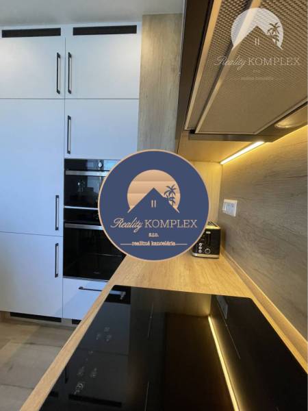 Vám ponúka na Prenájom 2-izbový byt s loggiou  - Kuchyňa v 2-izbovom byte s bielymi skrinkami a podlahou s dreveným dekorom.