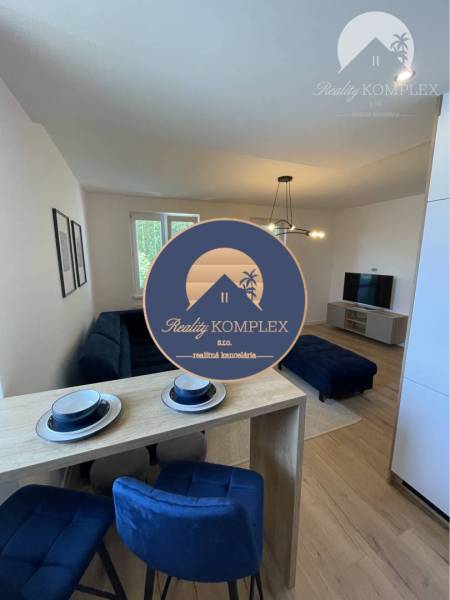 Vám ponúka na Prenájom 2-izbový byt s loggiou  - Obývačka v 2-izbovom byte s podlahou s dreveným dekorom a modrým nábytkom.