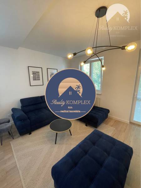 Vám ponúka na Prenájom 2-izbový byt s loggiou  - Obývacia izba s tmavomodrými sedačkami a podlahou s dreveným dekorom v 2-izbovom byte.