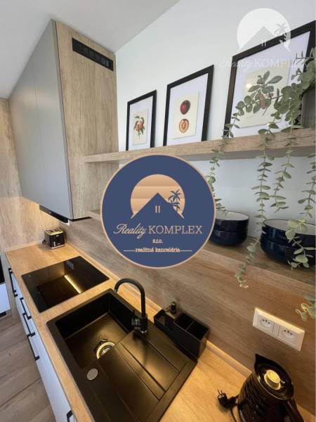 Vám ponúka na Prenájom 2-izbový byt s loggiou  - Kuchyňa v 2-izbovom byte s dreveným dekorom, čierny drez a dekoračné obrázky.