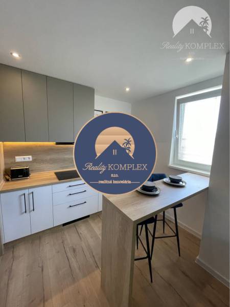 Vám ponúka na Prenájom 2-izbový byt s loggiou  - Kuchyňa v 2-izbovom byte s barovým pultom a podlahou s dreveným dekorom.