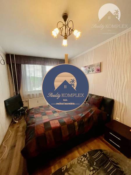 Vám ponúka 3-izbový byt s loggiou po kompletnej - Spálňa v 3-izbovom byte s podlahou s dreveným dekorom, posteľou a televízorom.