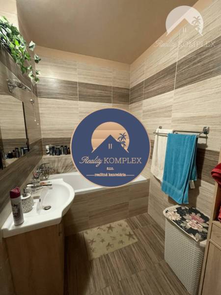 Vám ponúka 3-izbový byt s loggiou po kompletnej - Kúpeľňa v 3-izbovom byte s vaňou a podlahou s dreveným dekorom, obklopená doplnkami.