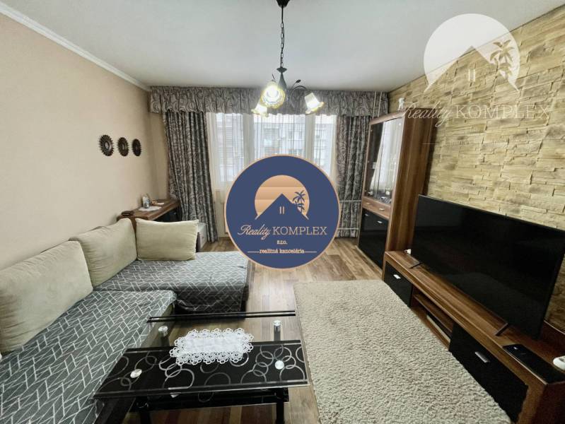 Vám ponúka 3-izbový byt s loggiou po kompletnej - Obývacia izba v 3-izbovom byte so sedačkou, televízorom, podlahou s dreveným dekorom.