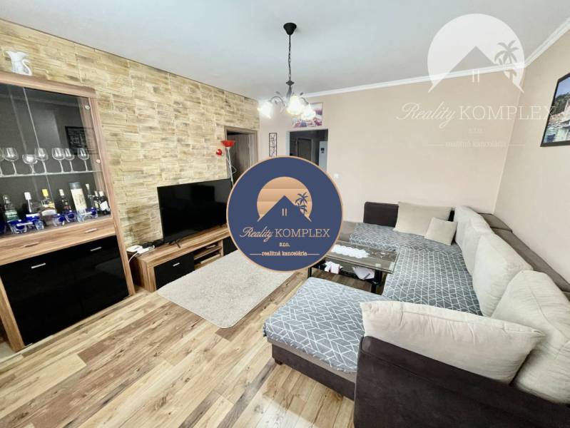 Vám ponúka 3-izbový byt s loggiou po kompletnej - Obývačka v 3-izbovom byte s podlahou s dreveným dekorom a rohovou sedačkou.