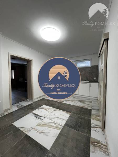 Vám ponúka na PREDAJ kompletne zrekonštruovaný  - Interiér rodinného domu s dlaždicovou podlahou, bielymi stenami a kuchynskou linkou.