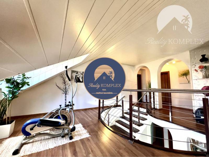 Ponúka na PREDAJ zrekonštruovaný 5 izbový podpi - Interiér rodinného domu s cvičebným strojom, schodisko a dekorácie na stene.