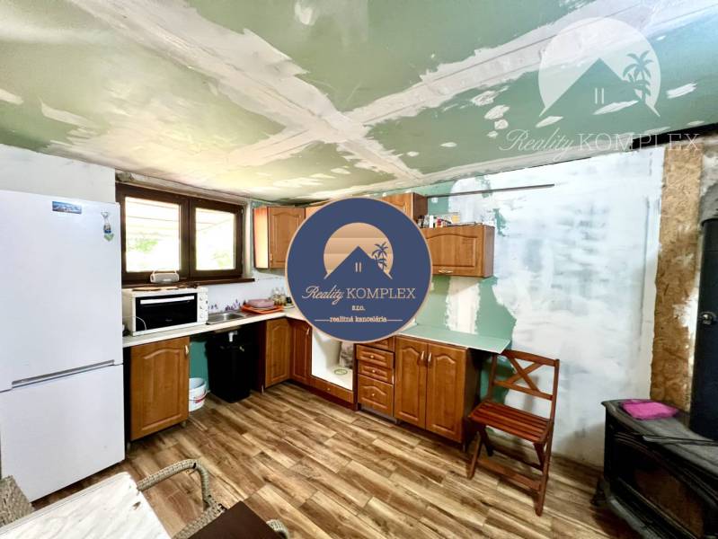 Ponúka na PREDAJ viničný domček s priestranným  - Kuchyňa v Chate s drevenou podlahou, chladničkou a hnedým nábytkom.