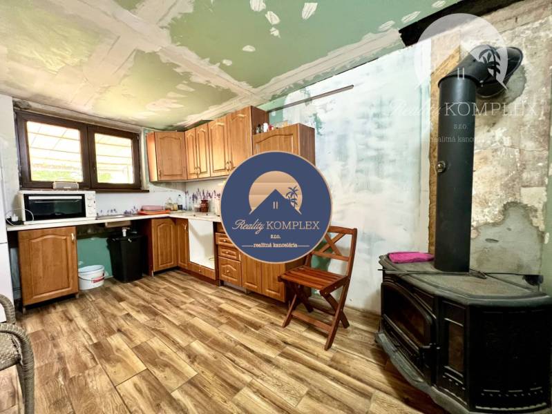 Ponúka na PREDAJ viničný domček s priestranným  - Kuchyňa v chate s drevenými skrinkami a pecou, vhodná pre pobyt v prírode.