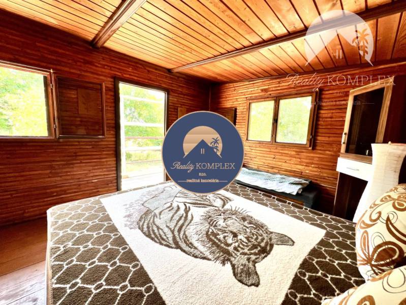 Ponúka na PREDAJ viničný domček s priestranným  - Izba v chate s drevenými stenami a posteľou, svetlo vstupuje cez okná.