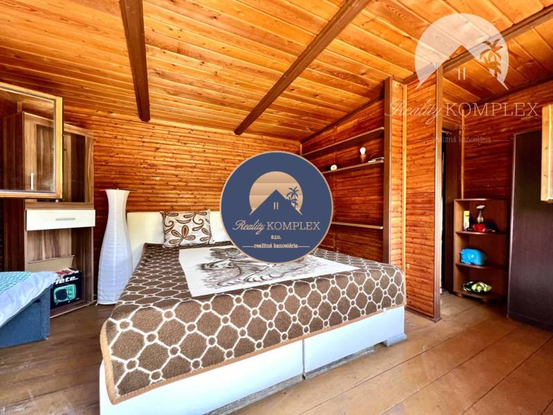 Ponúka na PREDAJ viničný domček s priestranným  - Drevený interiér chaty s posteľou a skriňou v útulnom priestore.