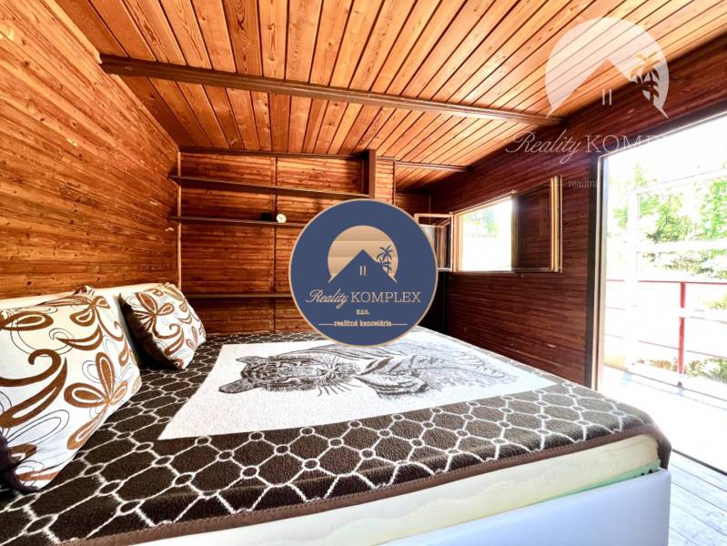 Ponúka na PREDAJ viničný domček s priestranným  - Drevený interiér chaty s posteľou a oknom.