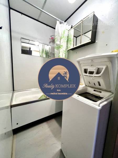 Ponúka na PREDAJ 1 izbový byt v Komárne - Kúpeľňa so sprchovacím kútom a práčkou v 1-izbovom byte s bielymi stenami.