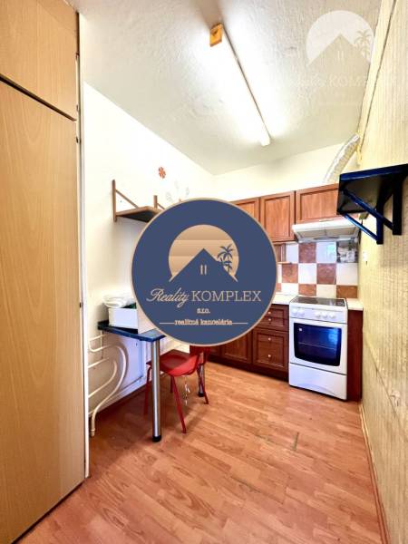 Ponúka na PREDAJ 1 izbový byt v Komárne - Kuchyňa v 1-izbovom byte s podlahou s dreveným dekorom a plynovým sporákom.