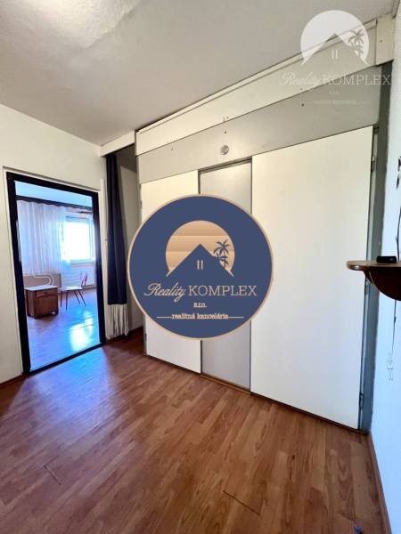 Ponúka na PREDAJ 1 izbový byt v Komárne - Interiér 1-izbového bytu s podlahou s dreveným dekorom a vstavanou skriňou.