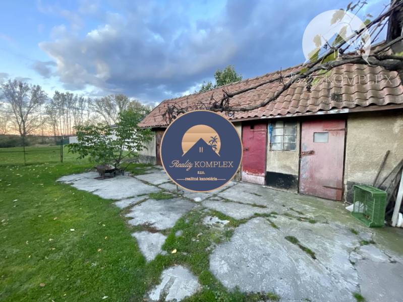 Investičný pozemok s obývateľným domom vo Vrakúni - Rodinný dom vo Vrakúni s vedľajšou budovou a trávnatým pozemkom, obloha s oblakmi.